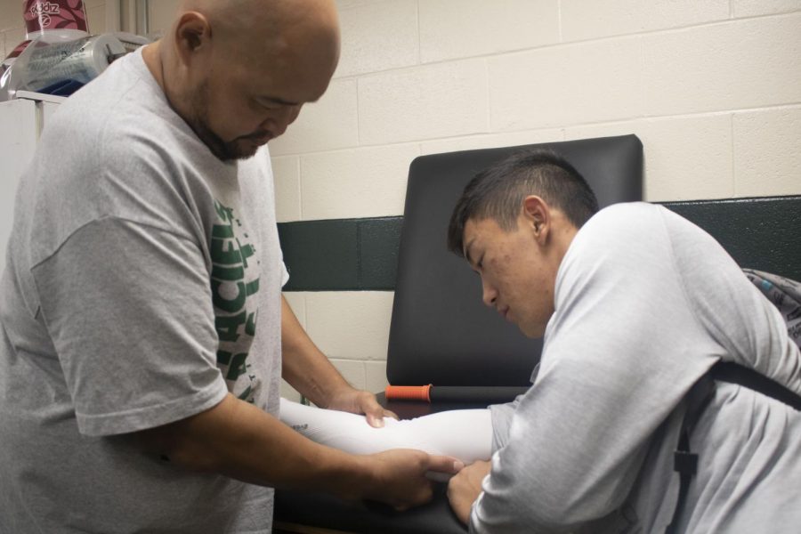 Trainer Joel Jaucian rolls out 11th grader Mackenzie Higuchi's forearm to prevent further pain.