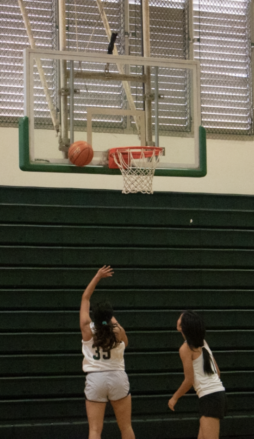 Girls varsity basketball team members Zannah Suehiro shoot the ball during practice, while Madi Sagawa rebounds. The team has improved their record since last year under a new coach. 