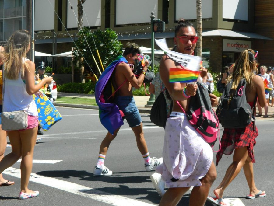 Person waves flags down the streets of Waikiki during Honolulu Pride 2018.