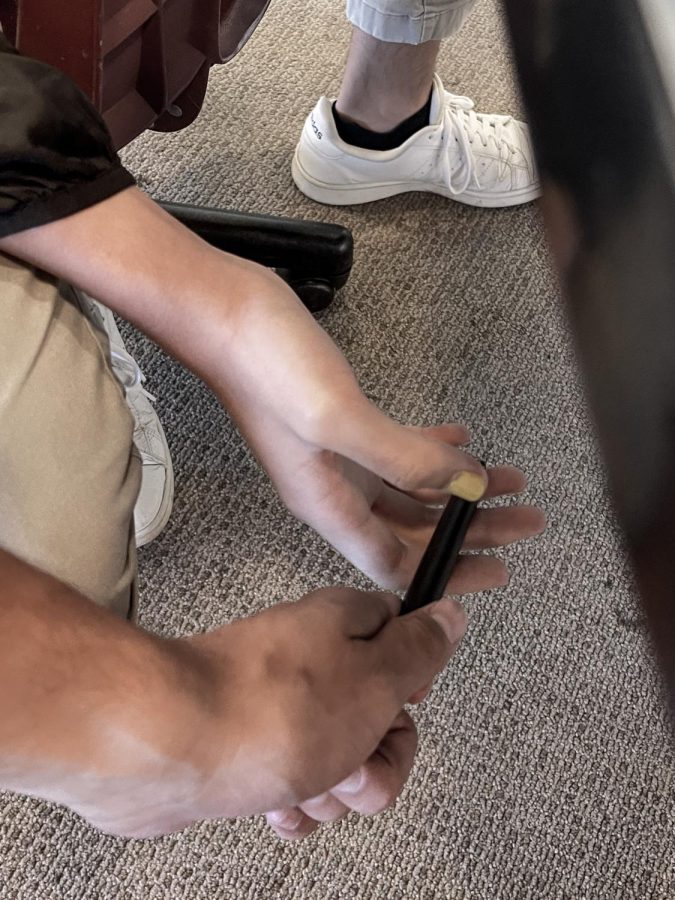 Two students discreetly pass a "vape" under the table, staged.